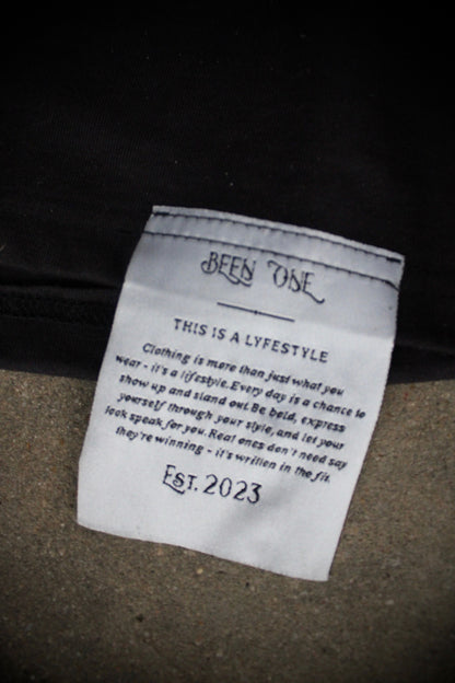 Tag on a black Dinamik Tee with a white label showing “Est. 2023”.